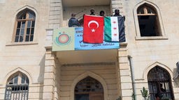 Von der Türkei unterstützte syrische Kämpfer halten eine türkische und eine syrische Flagge vom Ratsgebäude im kurdischen Afrin