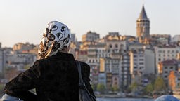Junge Frau mit Kopftuch schaut in Istanbul auf Beyoglu-Panorama mit Galata-Turm