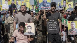 Syrien, Qamishli: Verwundete kurdische Kämpfer halten Bilder von Kameraden, die im Kampf gegen die Terrormiliz Islamischer Staat (IS) getötet wurden, während einer Demonstration gegen eine mögliche türkische Militäroffensive in die Höhe