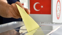 In eine Wahlurne wird ein Stimmzettel eingeworfen.
