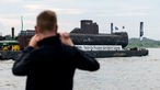 Das U-Boot auf einem Schwimmponton passiert auf dem Rhein den Ort Bimmen. Ein Mann fotografiert den Transport.