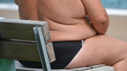 Übergewichtiger Mann sitzt am Strand