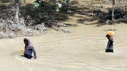 Personen waten durch ein überschwemmtes Gebiet, das durch die heftigen Regenfälle verursacht wurde, in Jangi Korona