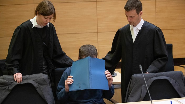  Bielefeld: Der Angeklagte sitzt mit einer Mappe vor dem Gesicht im Gerichtssaal neben seinen Verteidigern, Christina Peterhanwahr und Henning Jansen.