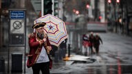 Ein verkleideter Mann geht im Regen mit einem Schirm über die Kö