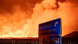 Ein Verkehrsschild mit Hinweis zur Blue Lagoon, im Hintergrund glühende Lava 