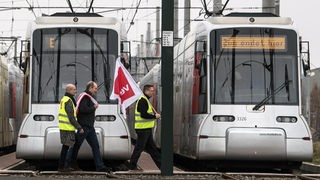 Mitarbeiter der Rheinbahn mit Verdi-Fahnen gehen über die Gleise vor ihren still stehenden Bahnen