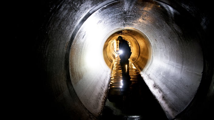 Ein Arbeiter schaut sich einen Wasserkanal unter der Erde an.