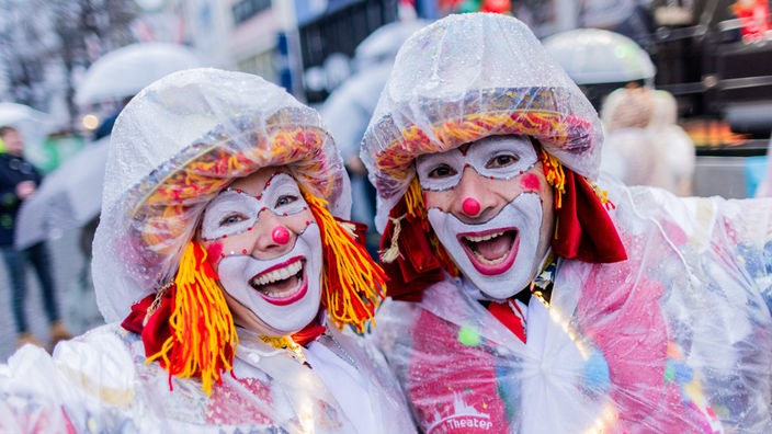 Karnevalisten mit Regenschutz feiern an Weiberfastnacht die Eröffnung des Straßenkarnevals auf dem Alter Markt.