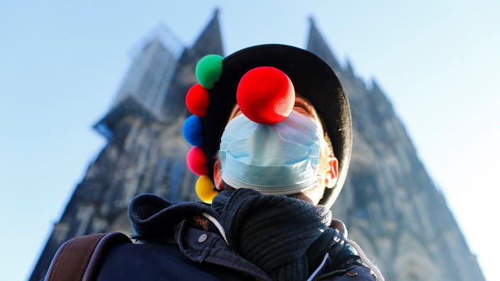 Ein Mann mit Maske und roter Clownsnase vor dem Kölner Dom.