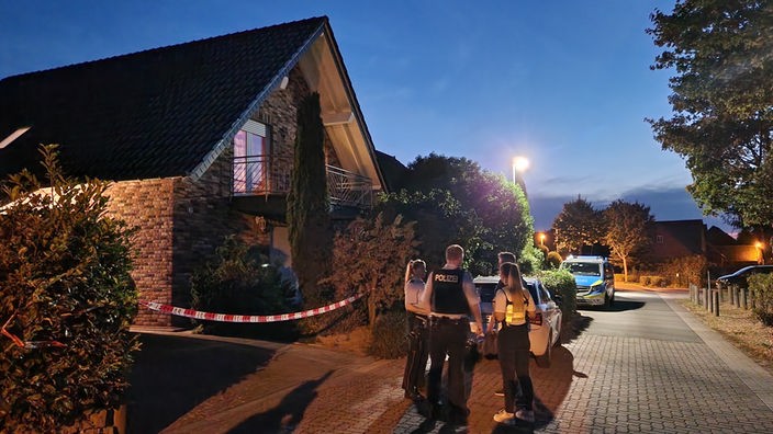 Polizisten stehen vor einem Einfamilienhaus