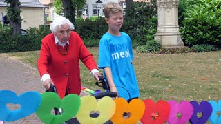 Frau Wübken, eine 98-jährige Frau mit weißen, kurzen Haaren, und Julian, ein blonder Junge, laufen nebeneinander her. 