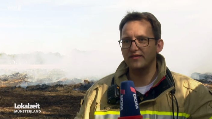 Felix Holling von der Feuerwehr Hopsten steht vor dem schwelenden Brand.