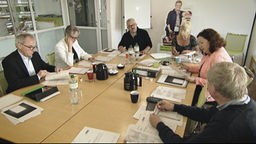 Sechs Menschen sitzen an einem Konferenztisch und studieren Unterlagen