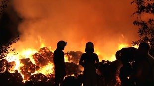 Brennende Strohballen mit Feuerwehrmännern im Vordergrund