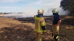 Zwei Feuerwehrmänner blicken auf ein verbranntes Feld.