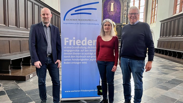Benedikt Kaleß, Lea Heuser, Dieter Spoo vor einem Banner mit der Aufschrift Aachener Friedenspreis. 