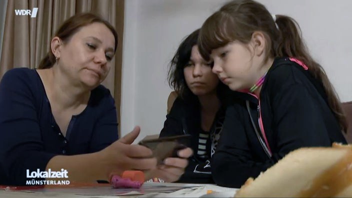 Alina, ihre Mutter und ihre Schwester schauen sich auf einem Handy Bilder aus der Ukraine an.