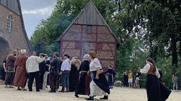 Viele mittelalterlich gekleidete Menschen stehen vor einem Fachwerk-Speicherhaus
