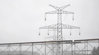 Eine Stromtrasse mit einem bodennahen Gerüst im Vordergrund.