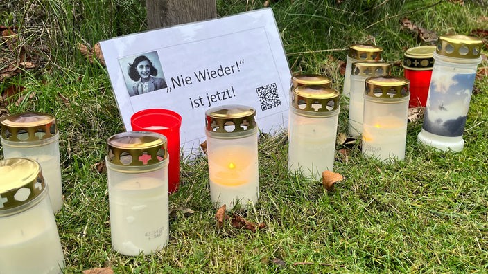 Kerzen stehen vor einem Bild von Anne-Frank mit dem Zitat "Nie Wieder! ist jetzt!"