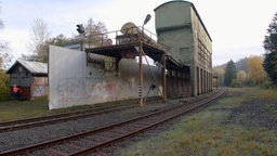 Eine Mauer und zwei Gebäude an Bahngleisen