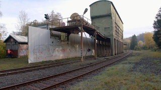 Eine Mauer und zwei Gebäude an Bahngleisen