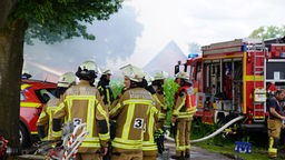 Feuerwehrleute stehen in einer Rauchwolke neben einem Feuerwehrwagen.