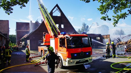 Ein Feuerwehrauto und viele Feuerwehrleute auf einem Bauernhof, die ein ausgebranntes Gebäude löschen