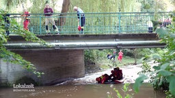 Männer auf einer Brücke halten mit einem Seil ein Schlauchboot mit Menschen im Wasser.