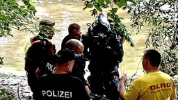 Ein Taucher steht am Ufer eines Flusses, umringt von mehreren Polizisten