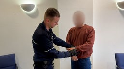 Täter in Handschellen vor Gericht, neben ihm steht ein Polizist