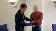 Täter in Handschellen vor Gericht, neben ihm steht ein Polizist