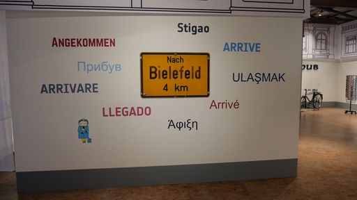 Eine Wand mit einem Schild auf dem "Nach Bielefeld 4km" steht.