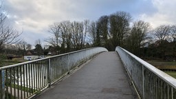 Es ist eine Fußgängerbrücke über den Kanal mit weißem Handlauf zusehen.