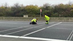 Zusehen sind zwei Männer, die den Fahrbahnbelag kontrollieren