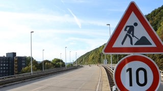 Neben einer leeren Autobahn stehen zwei Schilder, die auf eine Baustelle und Tempo 10 km/h hinweisen.