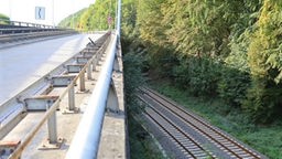 In der linken Bildhälfte ist eine Straßenbrücke zu sehen. In der rechten Bildhälfte verlaufen zwei Bahnschienen.