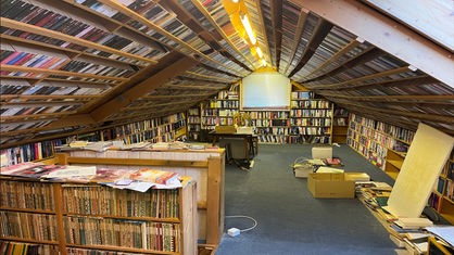 Ein Dachboden, auf dem sich viele Bücher in Regalen und unter der Decke befinden.