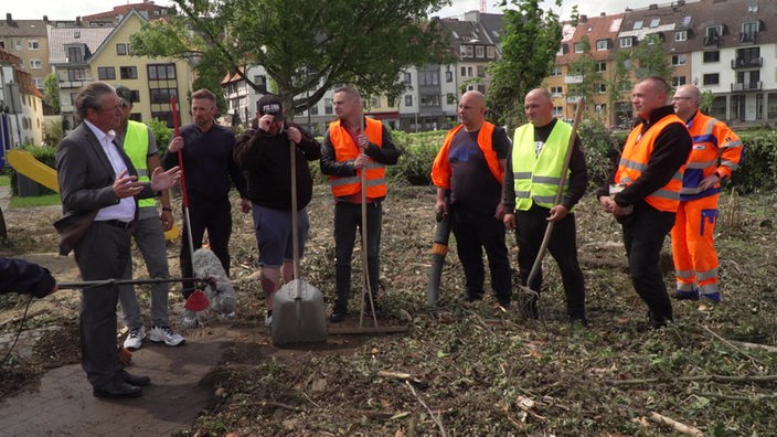 Der Bürgermeister von Paderborn steht zusammen mit acht polnischen Helfern in einem Park. Unter ihren Füßen wird der Fußboden bedeckt von Ästen und Dreck.