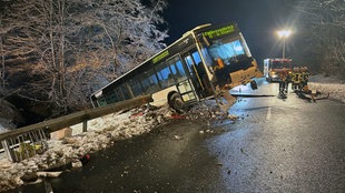 Ein Bus ist rückwärts durch eine Leitplanke gebrochen und ragt nun in die Luft.