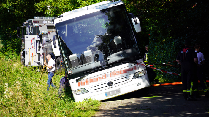 Der Reisebus in Schieflage, daneben Feuerwehrleute