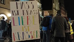 Junge Frau steht mit Schild vorm Rücken auf dem Prinzipalmarkt, darauf die Botschaft "Hass ist krass, Liebe ist krasser"