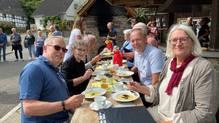 Menschen sitzen draußen an einem Tisch udn essen gemeinsam