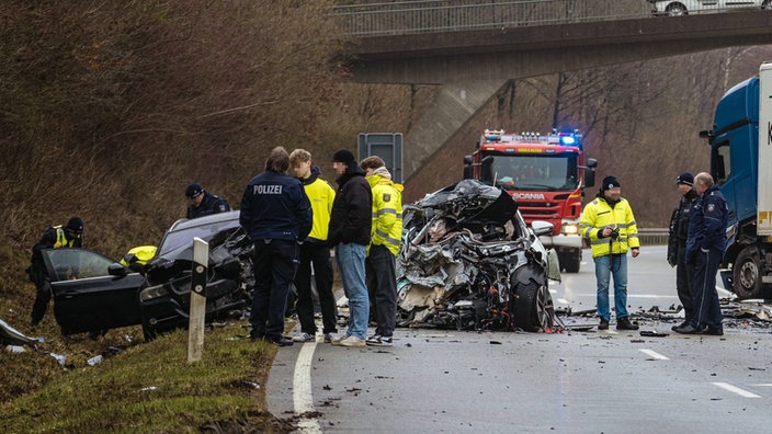 Mehrere Menschen und Rettungskräfte stehen neben zerstörten Autos. 