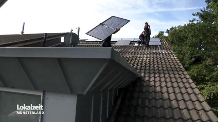 Zwei Männer bringen auf einem Hausdach Solaranlagen an. 