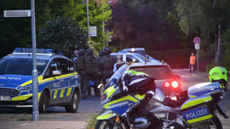 Hinter einem Polizeimotorrad steht eine Gruppe SEK-Beamter an einer Straße.