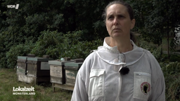 Karina Möllers steht im Imkerinnen-Anzug vor den Brutkästen ihrer Bienen.
