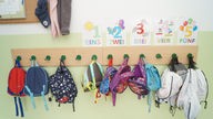 Das Bild zeigt die Garderobenhaken in einer Kita, an den Haken hängen Kinder-Rucksäcke.