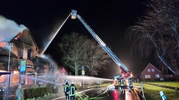 Seitenansicht der Feuerwehrkräfte mit Wasserschläuchen vor der brennenden Fassade des Ausflugslokals in Nordwalde.